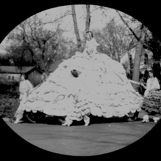 Parade float that is a woman wearing a very frilly and wide hoop skirt.